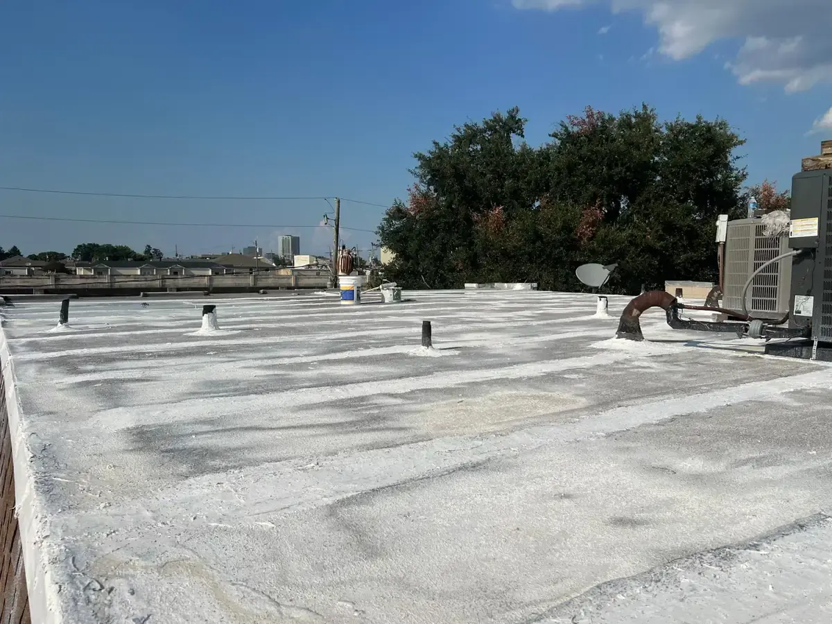 White coating being applied across a low-slope roof around equipment and pipes