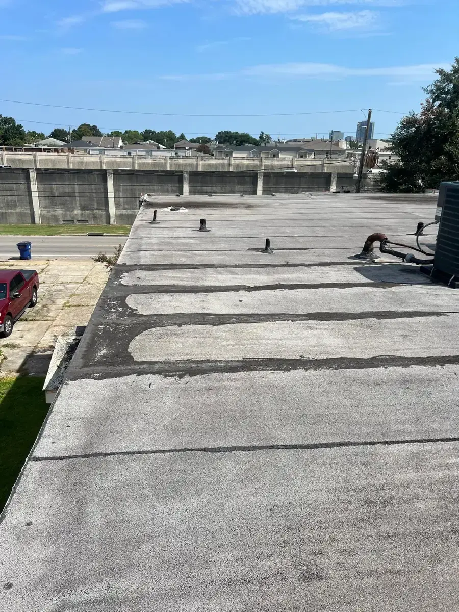 Low-slope roof with dark repair bands along seams and several pipe penetrations