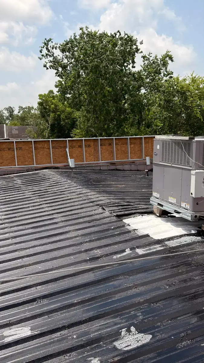 Dark-treated metal roof surface around rooftop equipment and a perimeter wall