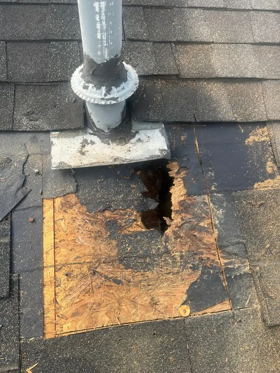 Hole and deteriorated roof decking below a metal pipe flashing