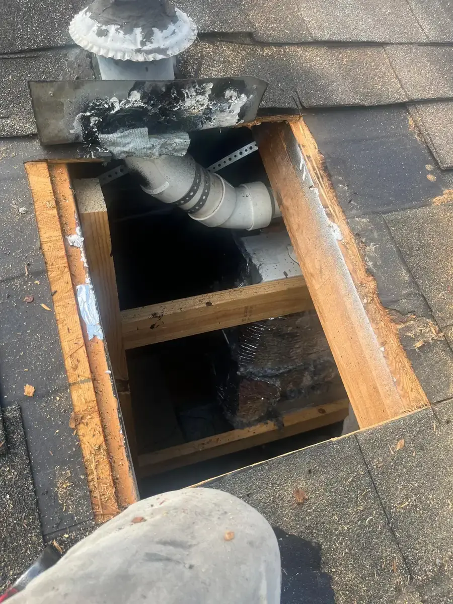 Rectangular opening in roof decking beside a pipe, with framing visible below